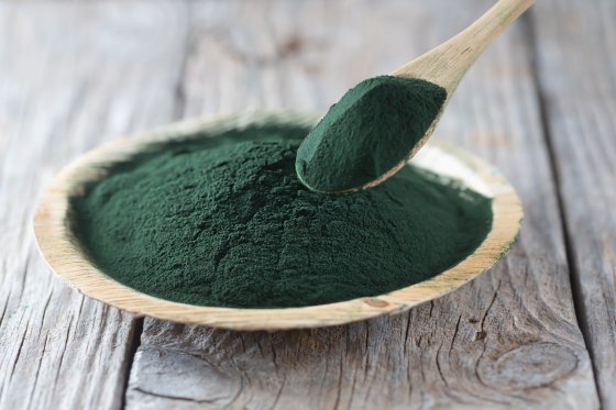 Spirulina als Pulver in einer Schale auf einem Holztisch