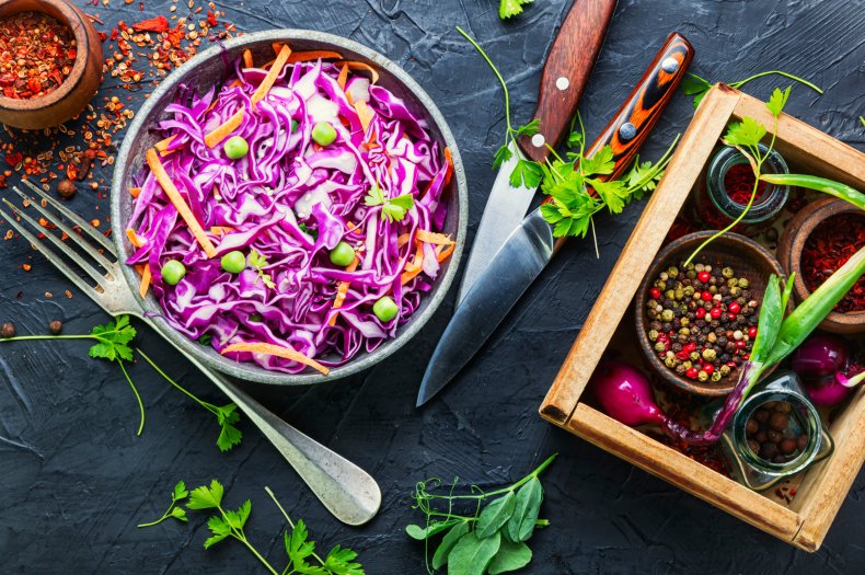 Rotkohlsalat mit Gem&uuml;se und Kr&auml;utern in einer Sch&uuml;ssel auf einem schwarzen Tisch