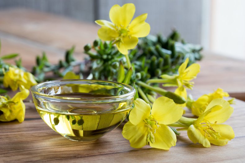 Huile d'onagre dans un bol en verre avec des fleurs d'onagre fraîches en arrière-plan.