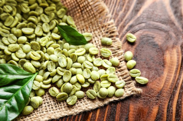 Gr&uuml;ner Kaffee wird aus einem Sack auf einen braunen Tisch geleert