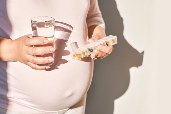 Schwangere Frau h&auml;lt ein Wasserglas in der einen und  Supplemente in der anderen Hand