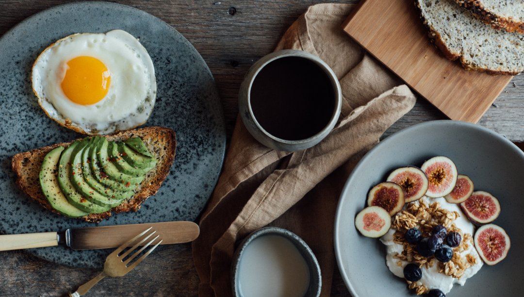 Frühstückstisch mit Avocado, Spiegelei, Brot und Porridge